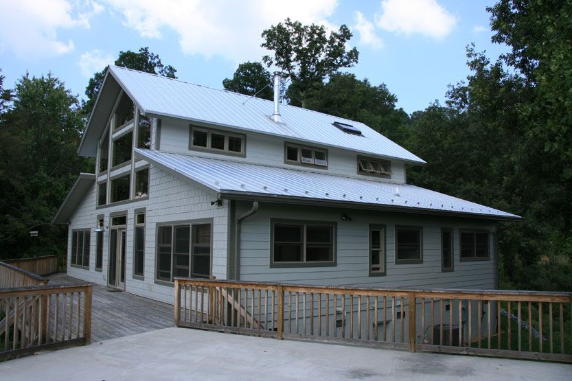A large white house with a metal roof is surrounded by trees.
