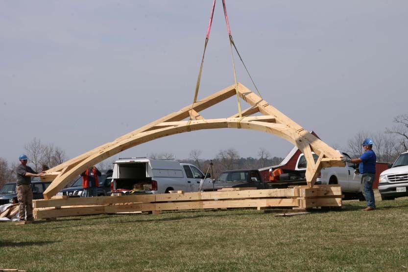 A crane is lifting a large piece of wood in a field.