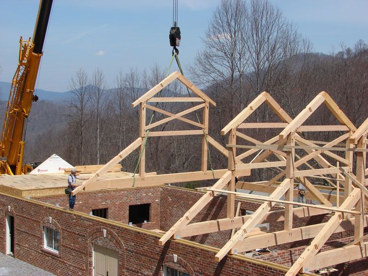 A crane is lifting a wooden structure on top of a brick building.