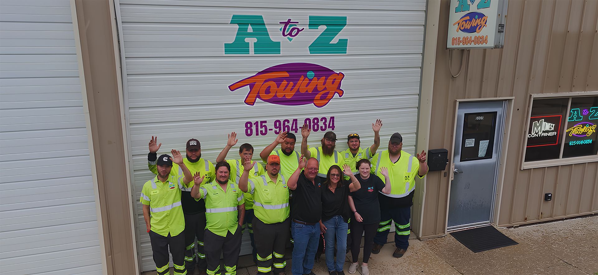 Group of people in neon safety vests, raising hands in front of a building with the words 