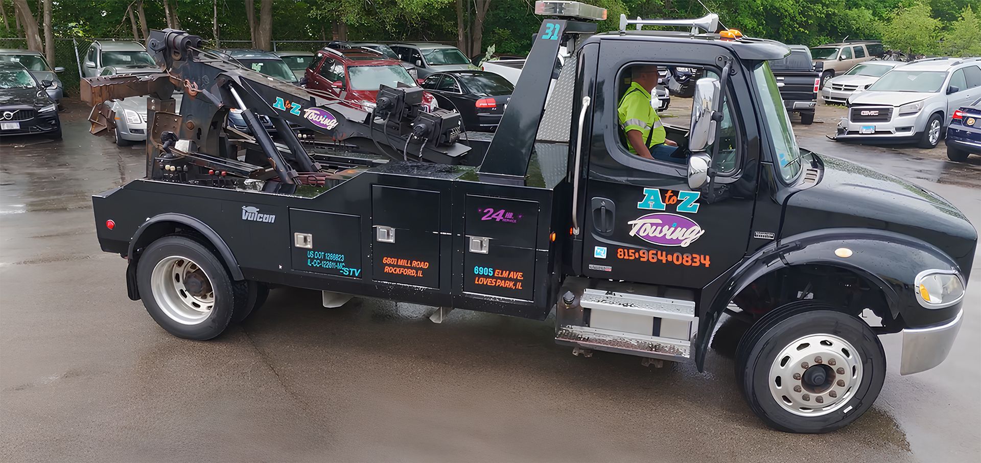 Black tow truck parked in a lot, driver inside.