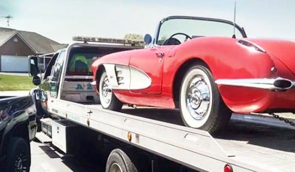 Red vintage convertible being towed on a flatbed tow truck.