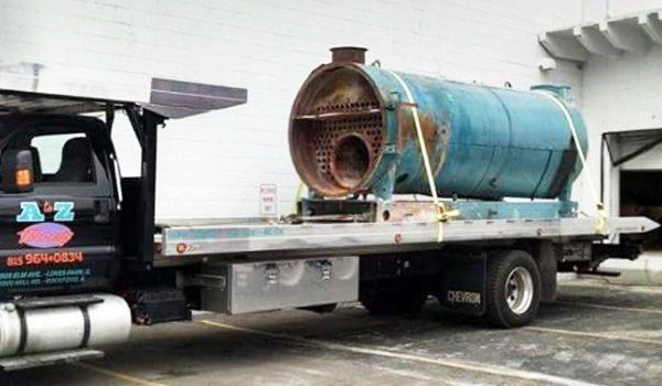 A large, teal industrial boiler strapped to a flatbed truck for transport, with a rusty interior visible.