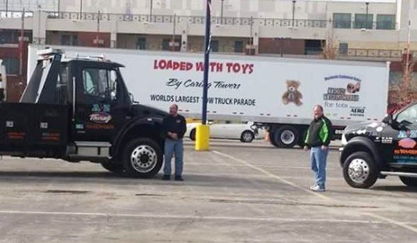Two men standing near tow trucks in a parking lot; a trailer reads 