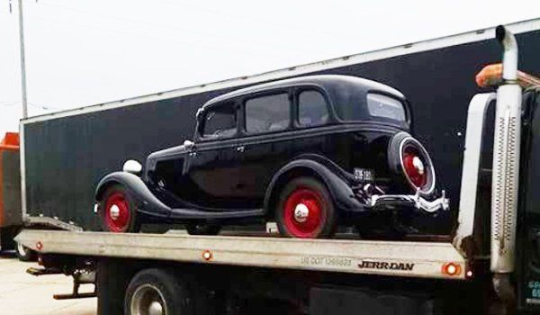 Black classic car with red wheels on a flatbed tow truck.