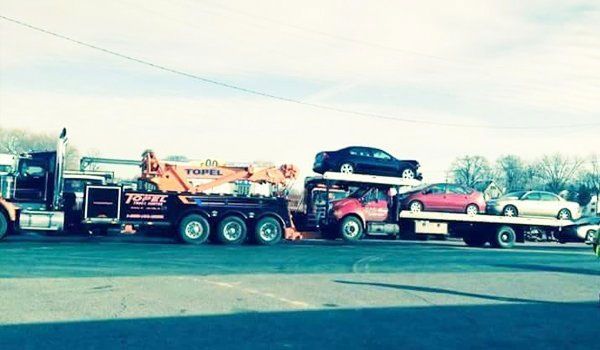 Tow trucks hauling multiple vehicles on a sunny day. A red pickup and three cars are loaded.