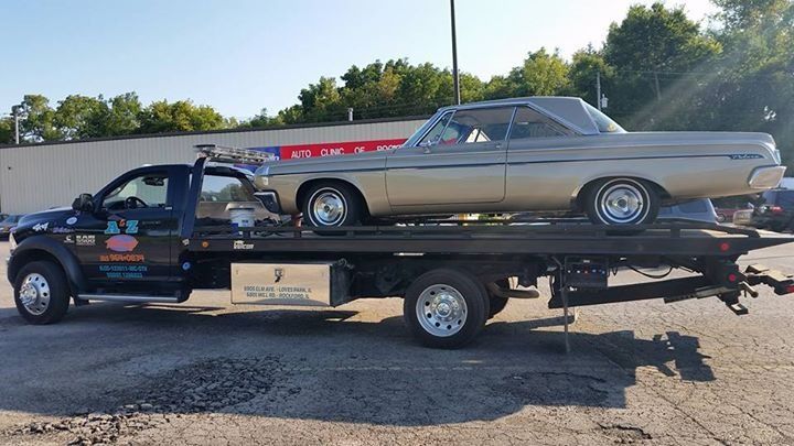 A classic car is being towed by a flatbed tow truck in an outdoor setting.