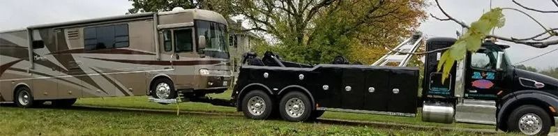 A motorhome is being towed by a black tow truck on a grassy field.