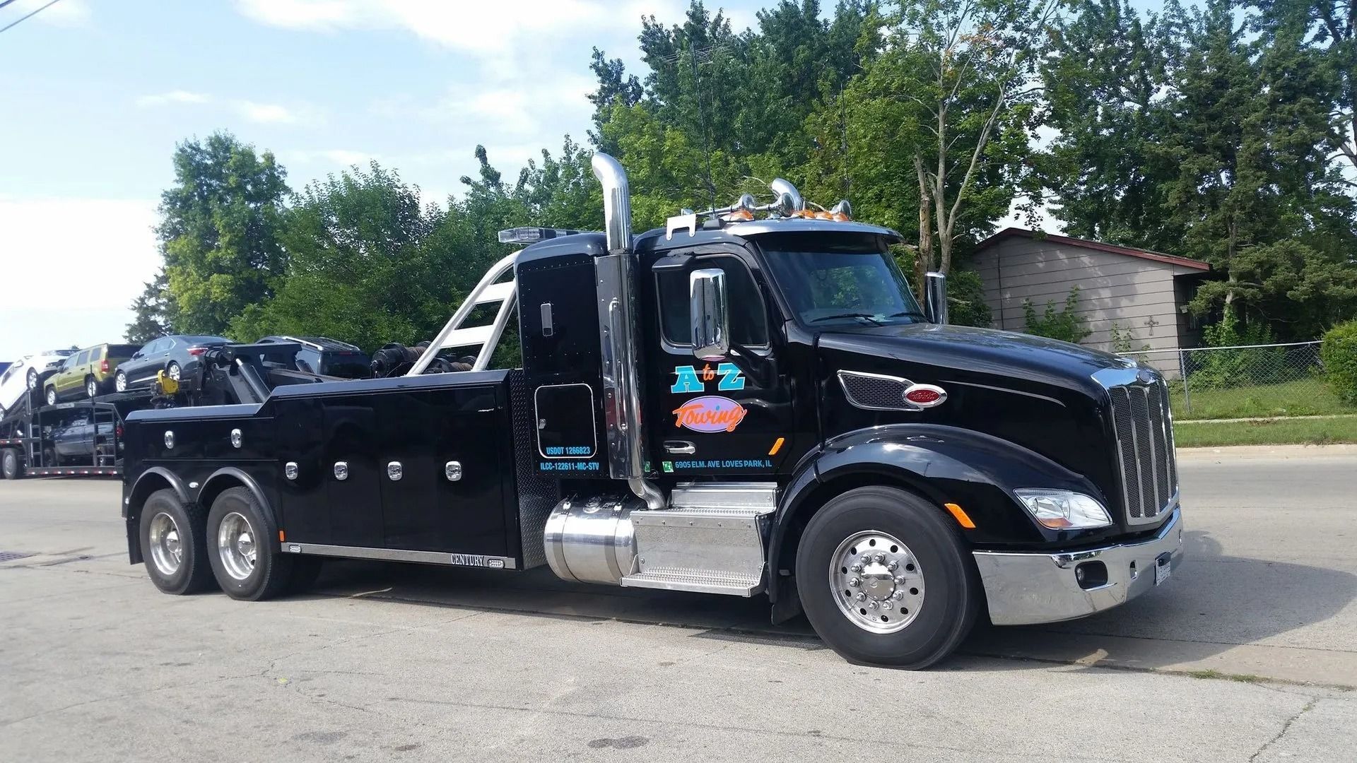Black tow truck parked on a street; trees and building in background.