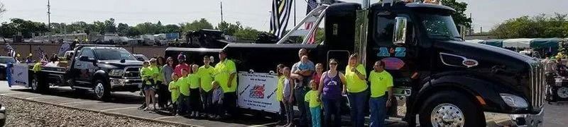 Group of people pose next to a black truck and trailers, some wearing neon yellow vests.