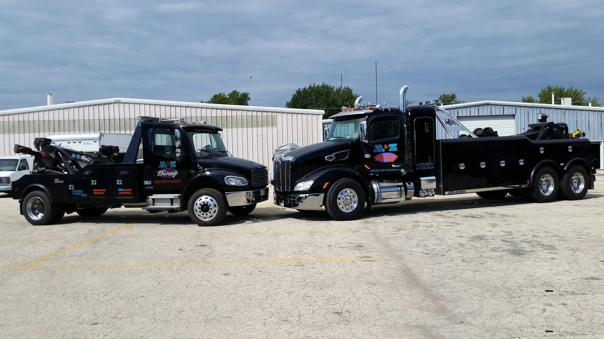 Two black tow trucks parked next to each other on a paved lot in front of a building.