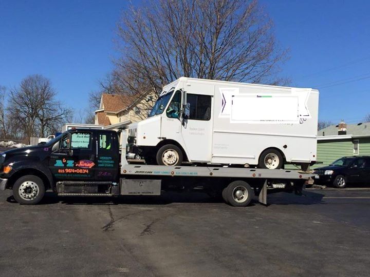 A white truck on a flatbed tow truck in a parking lot on a sunny day.