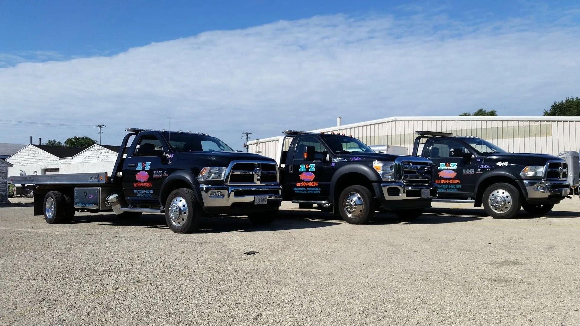 Three black tow trucks parked on gravel under a bright blue sky.