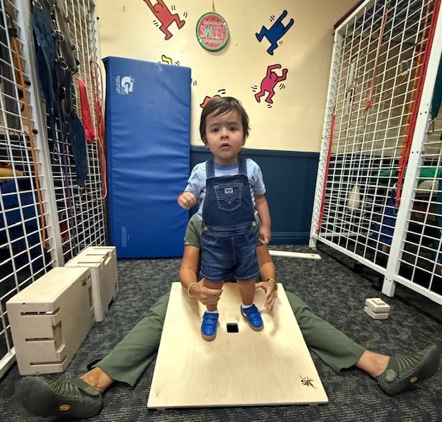toddler being helped to stand on a wooden platform by a woman