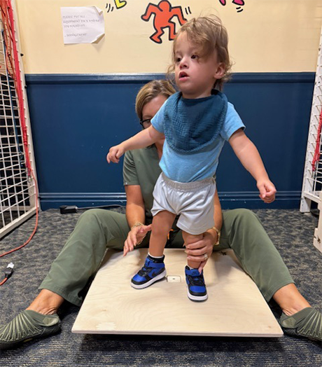 toddler being helped to stand on a wooden platform by a woman