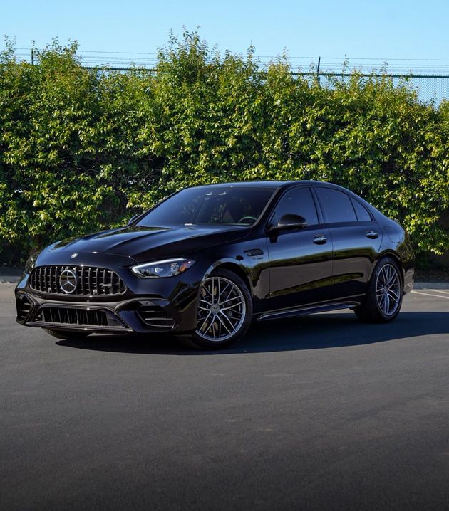 Black luxury sedan parked on pavement with green hedges in the background