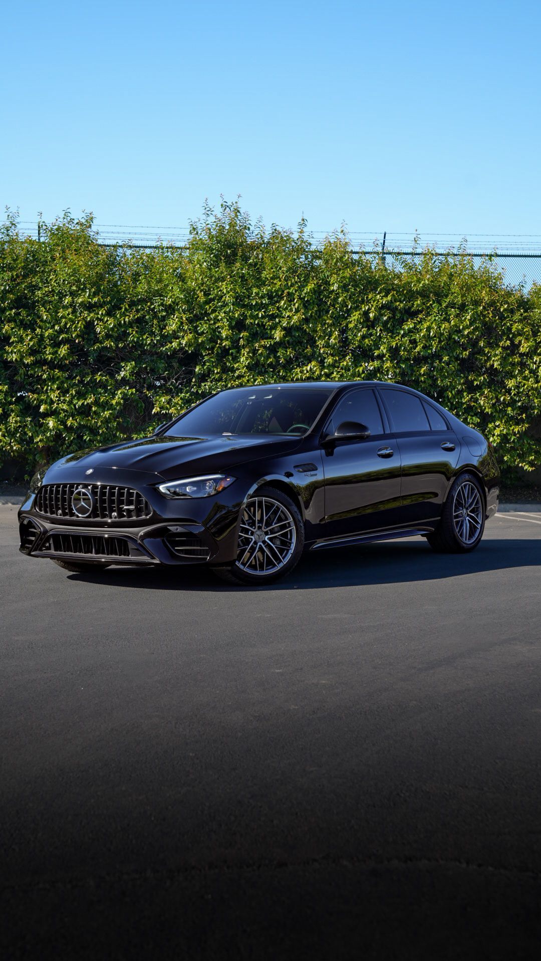 Black sports sedan parked on a paved road beside green hedges under a clear blue sky
