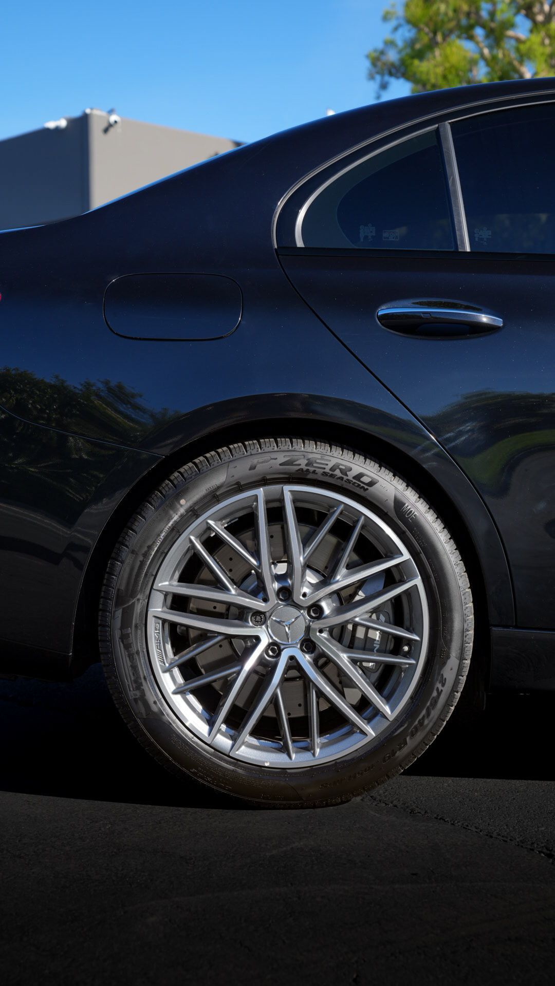 Close-up of a black sedan’s rear wheel with silver alloy rim parked outdoors.