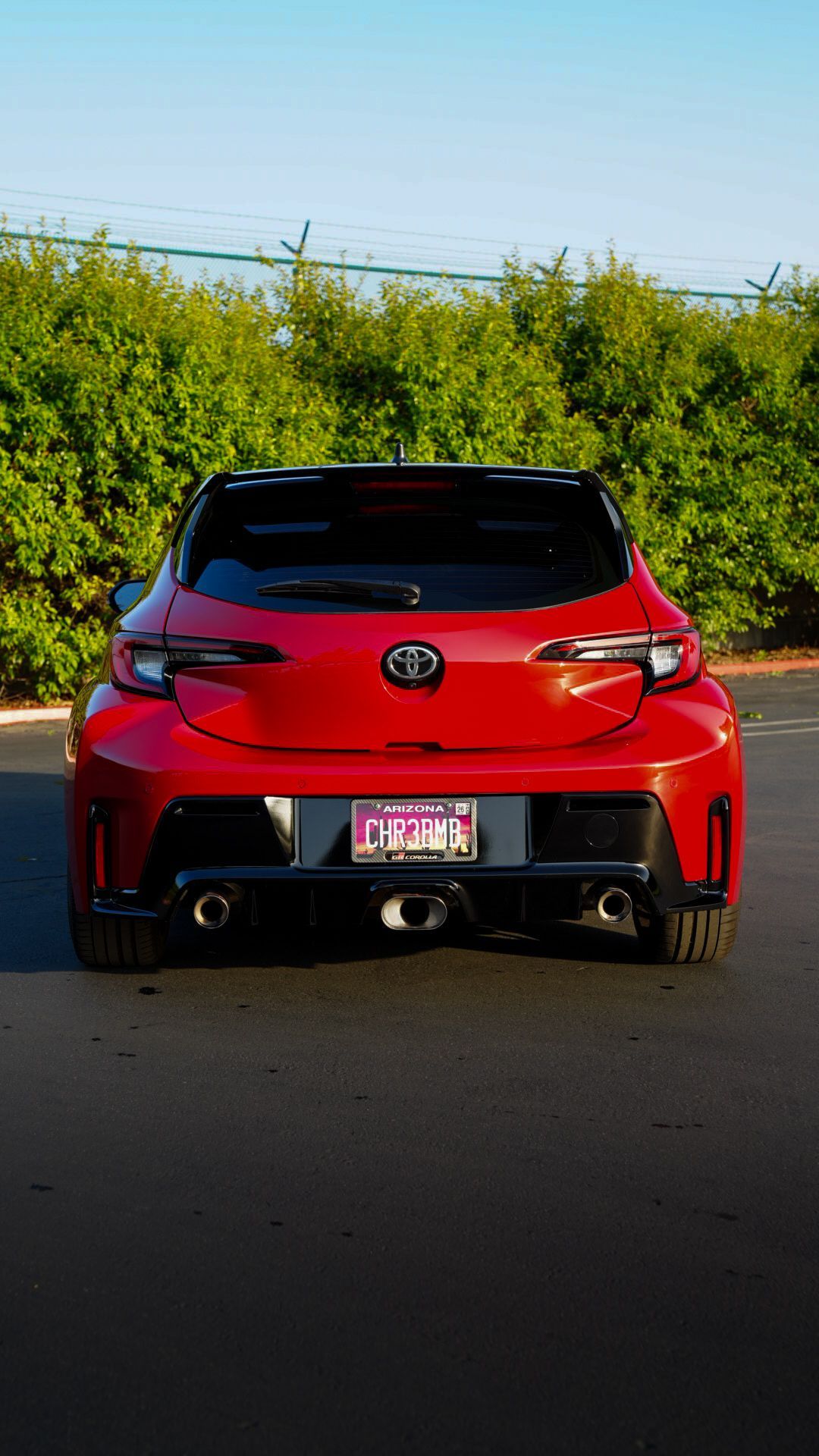 Red sports car seen from behind on a road with greenery and blue sky in the background