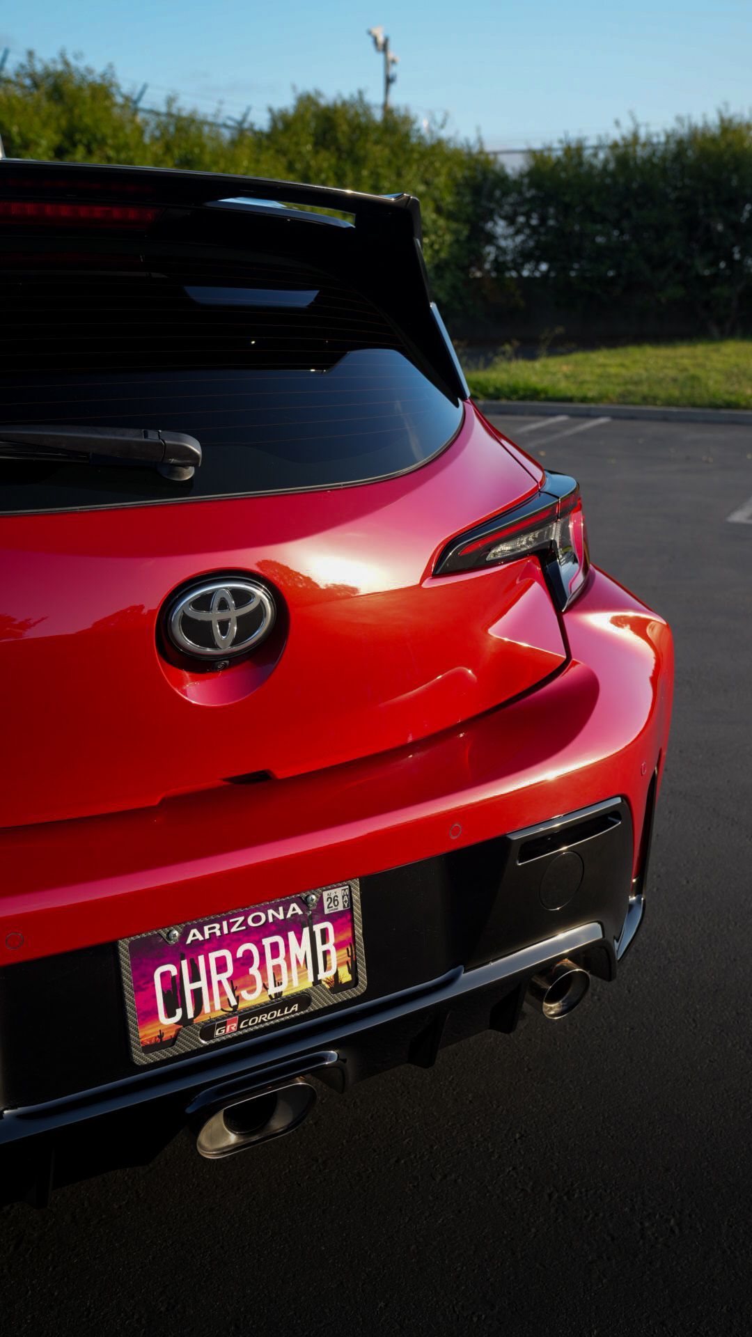 Rear view of a red Toyota hatchback with a custom license plate on a sunny road