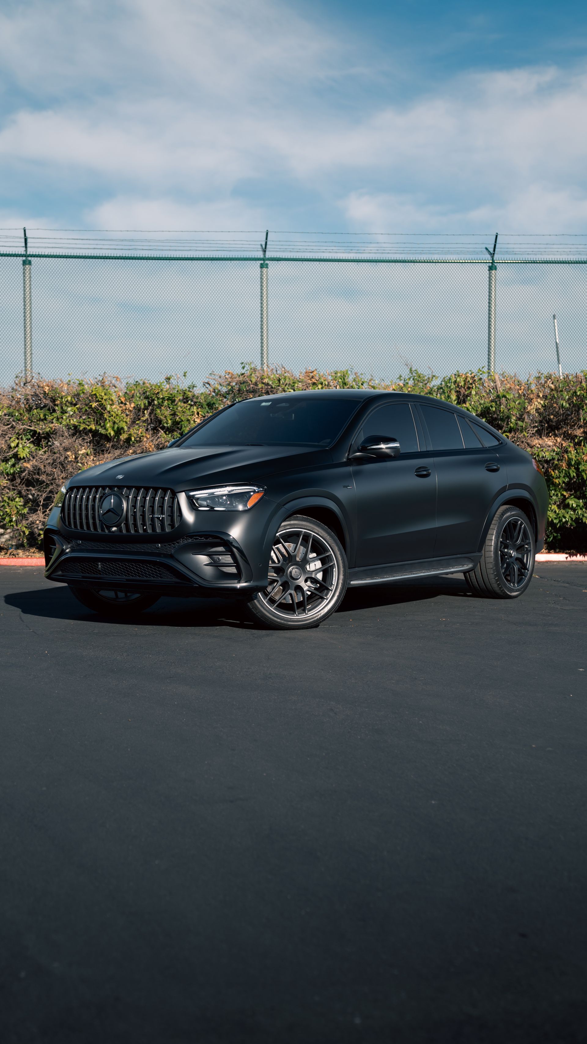 Black SUV parked on pavement beside a chain-link fence under a partly cloudy sky
