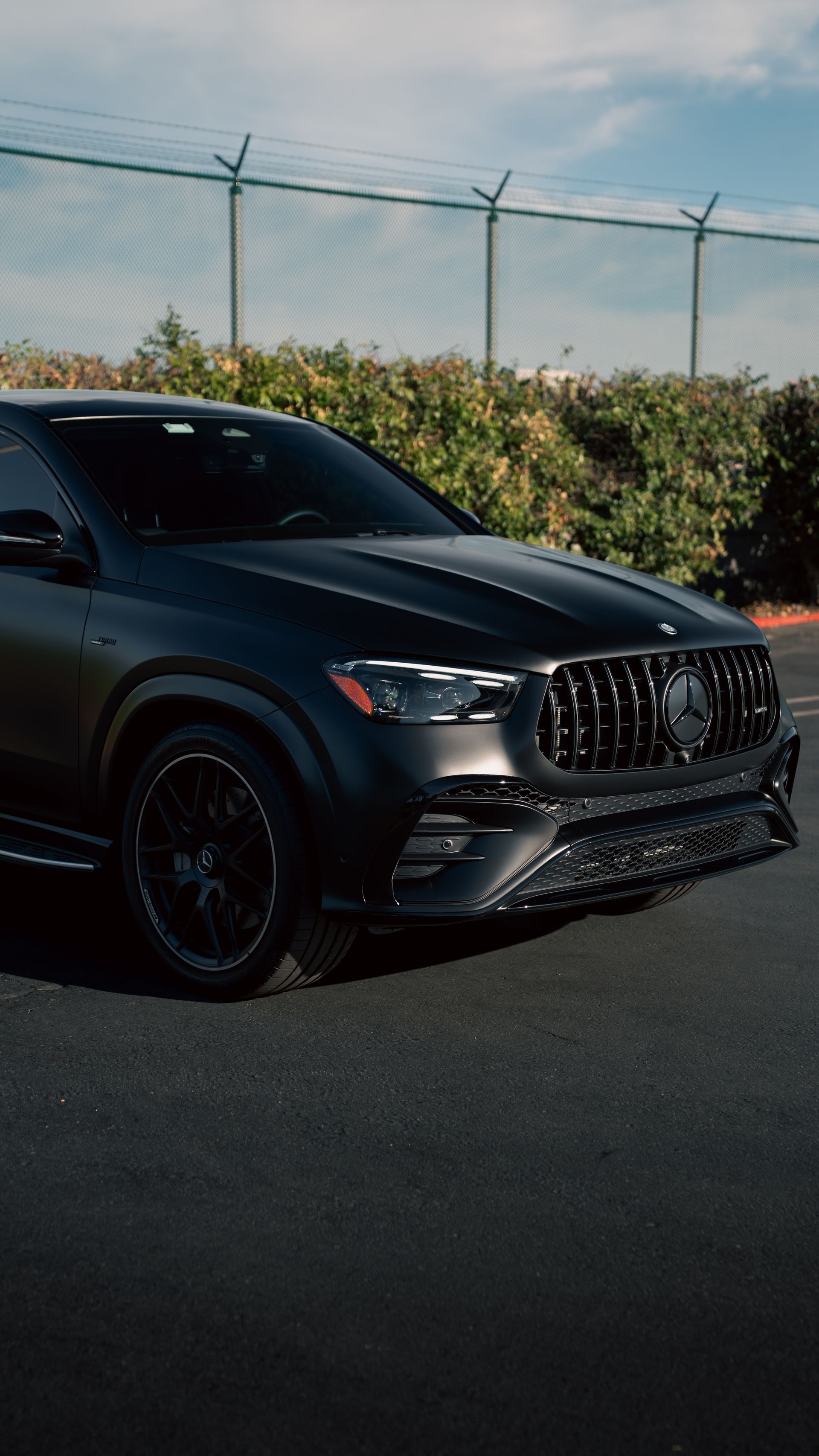 Black sports SUV parked on a road beside a fence under a blue sky