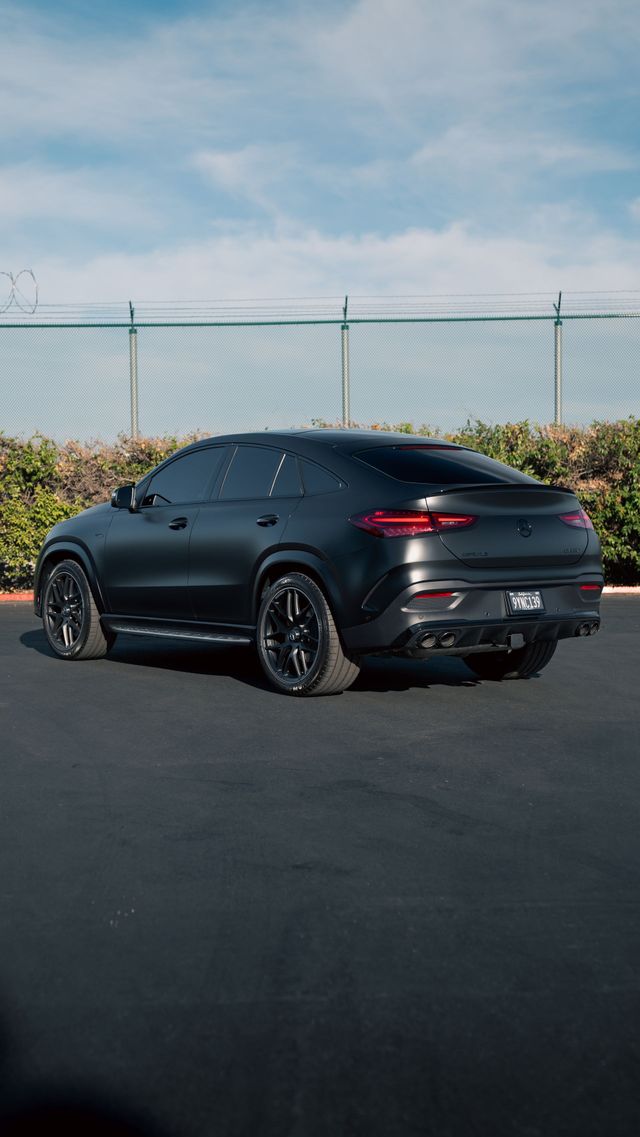 Matte black sporty SUV parked on asphalt near a chain-link fence under a blue sky