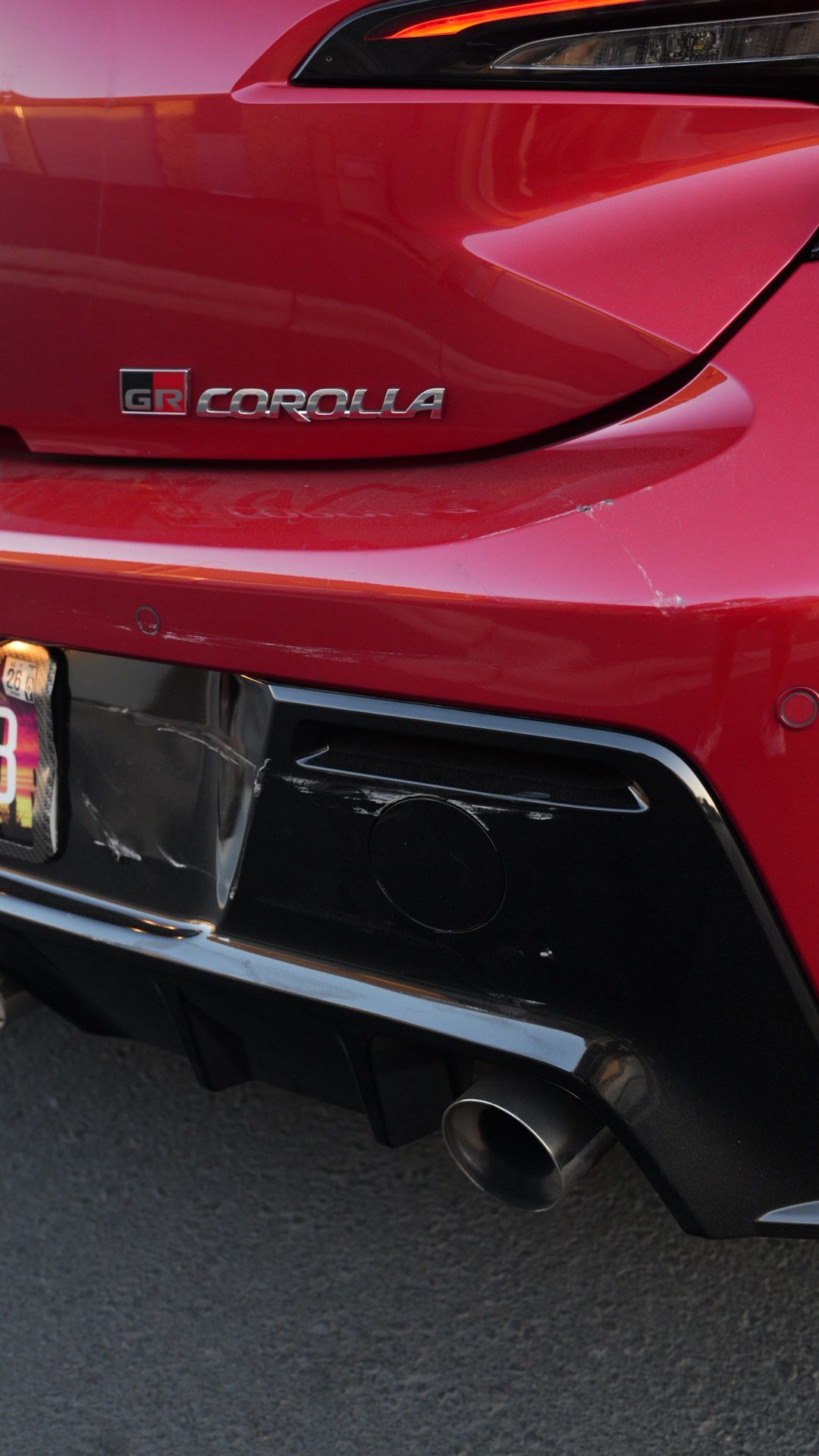 Rear view of a red Toyota Corolla with black bumper trim and a visible exhaust pipe.