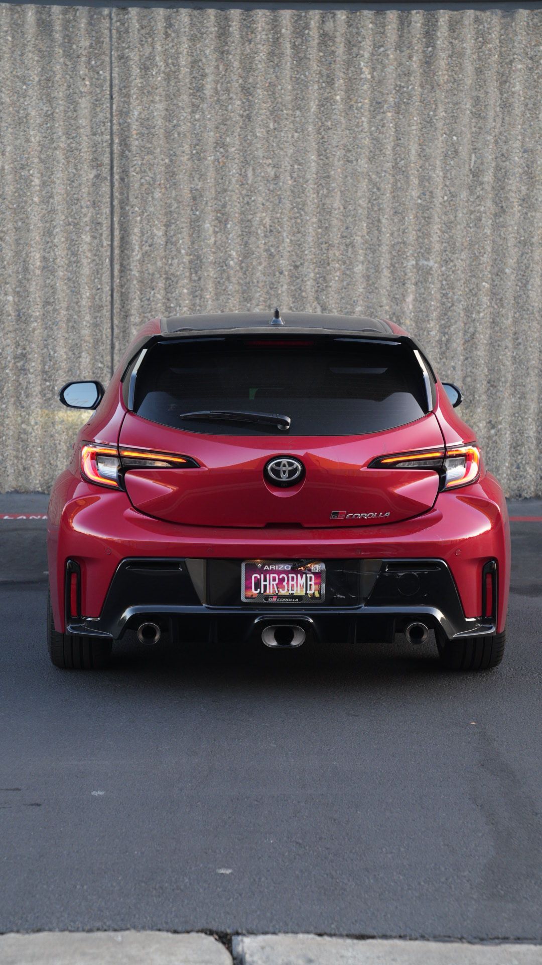 Rear view of a red Toyota sports car parked against a textured concrete wall.