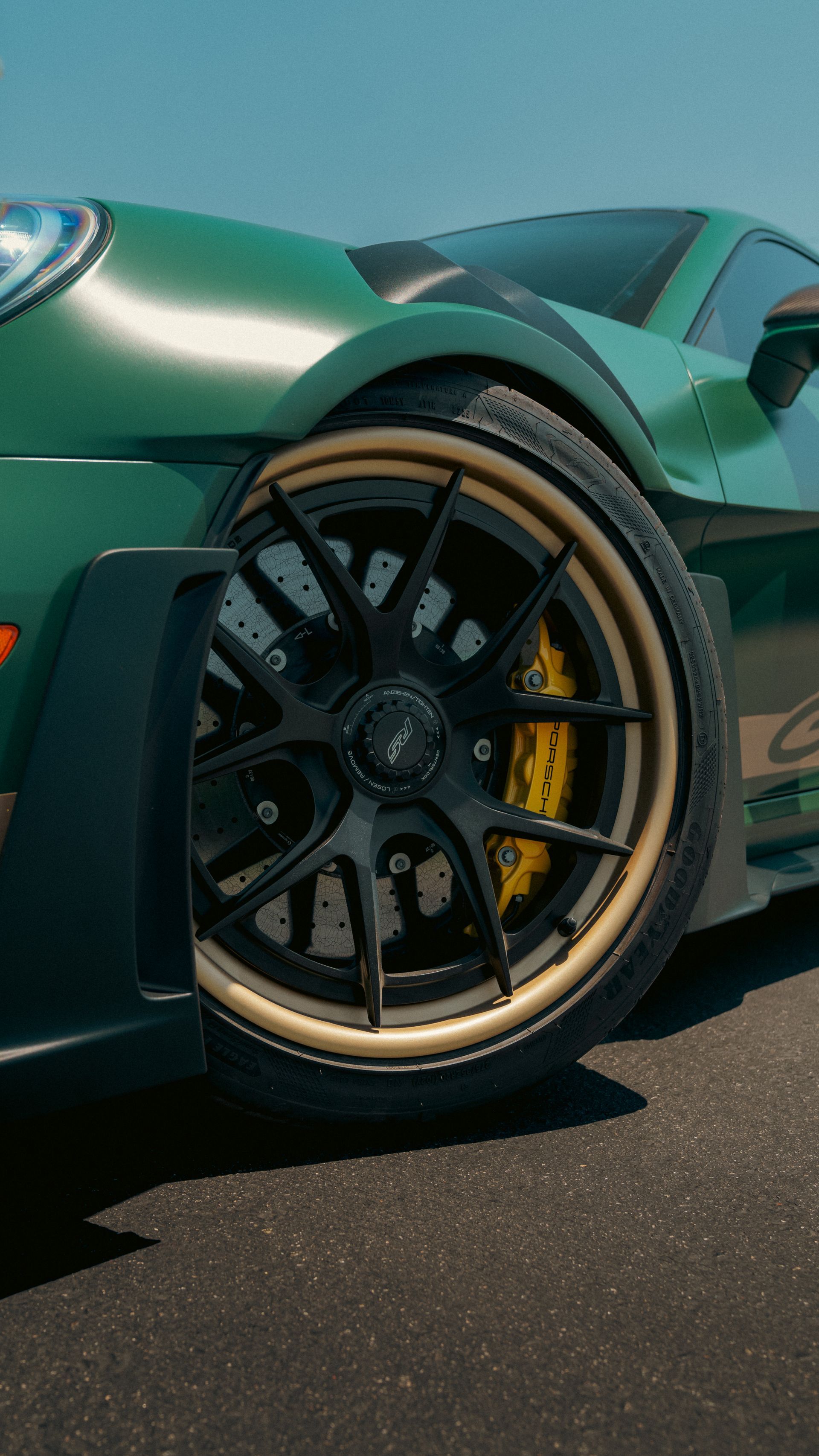 Close-up of a green sports car’s front wheel with black rims and yellow brake calipers.