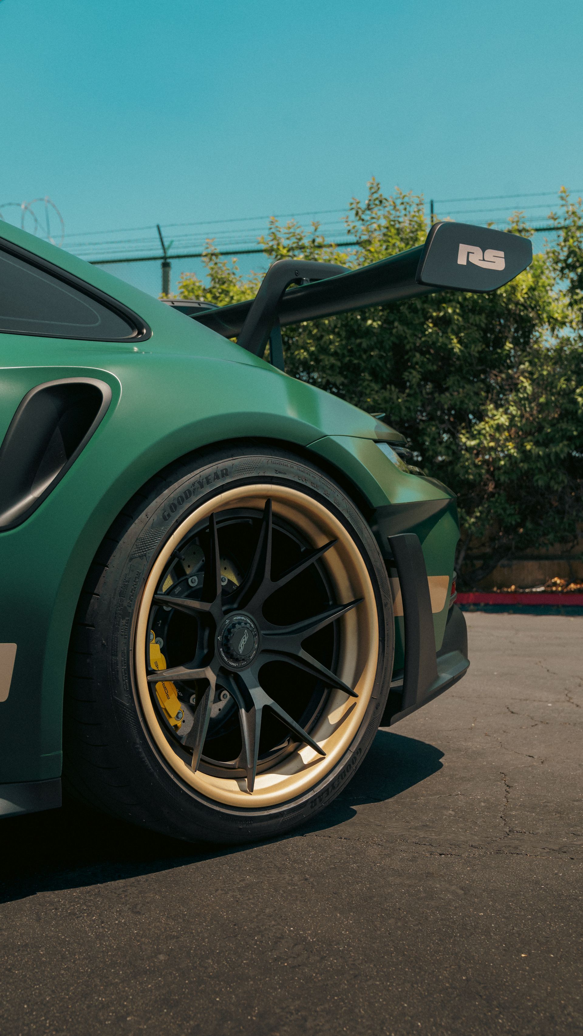 Green sports car with gold-rimmed wheel parked outdoors against a clear blue sky