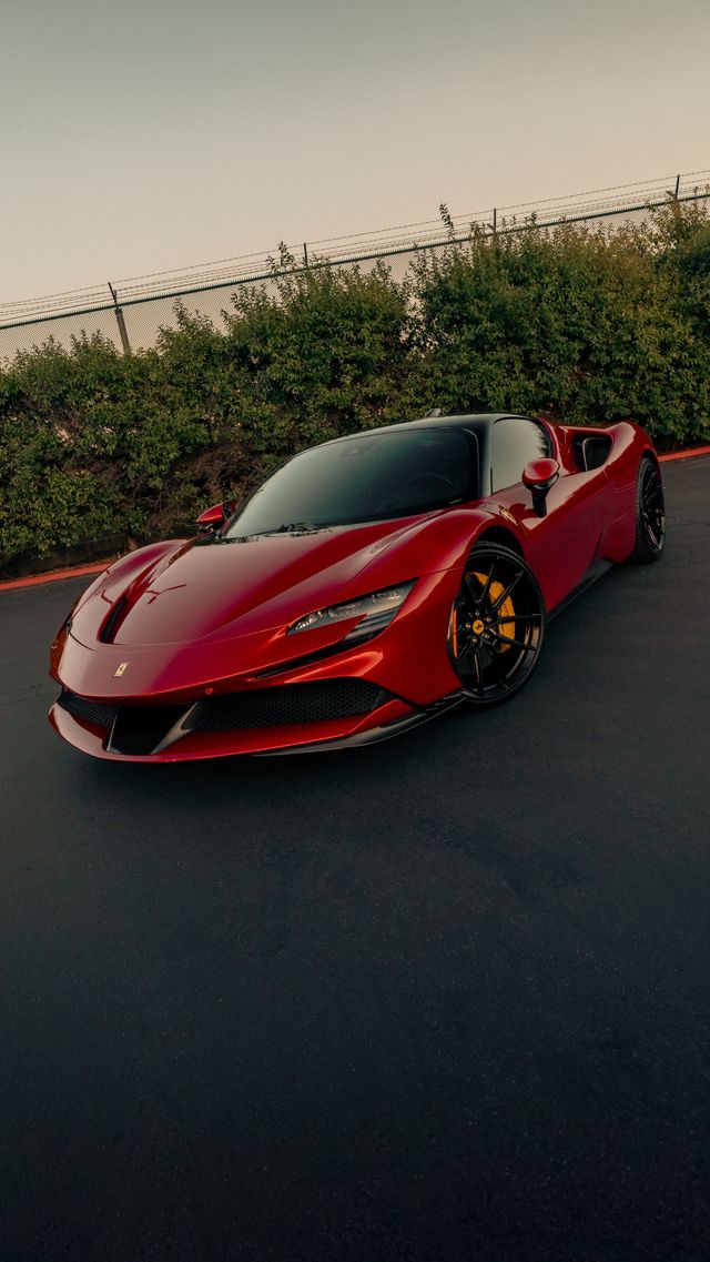 Red sports car parked on a road beside a hedge at sunset