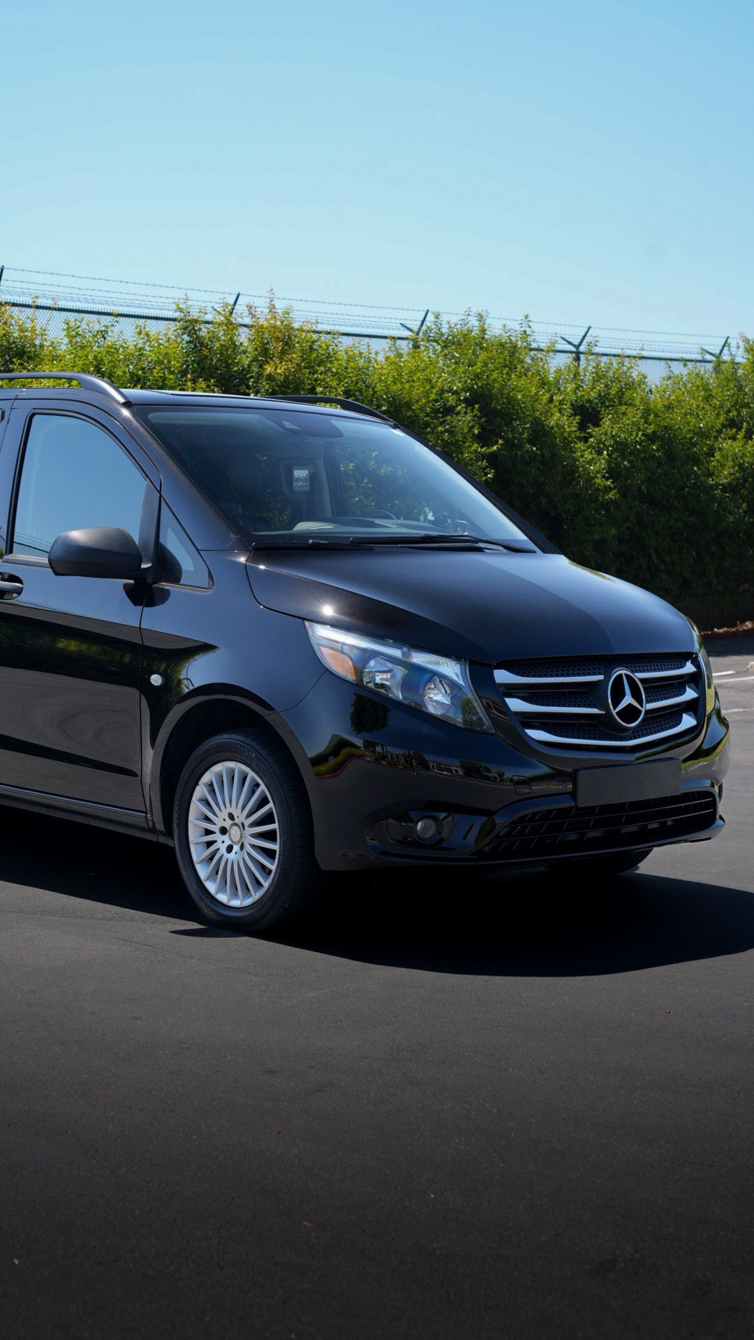 Black Mercedes van driving on a sunny road with green hedges in the background