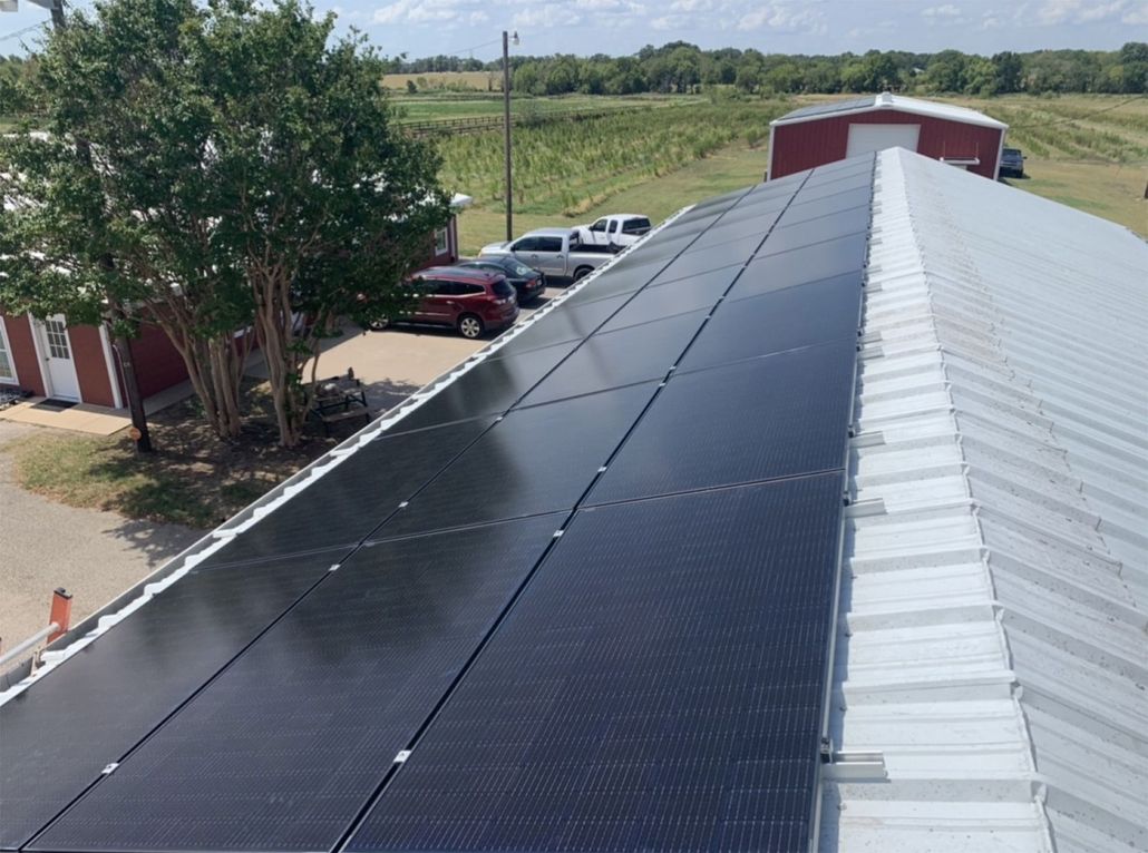 Solar panels installed along a red barn roof beside a rural driveway and fields.