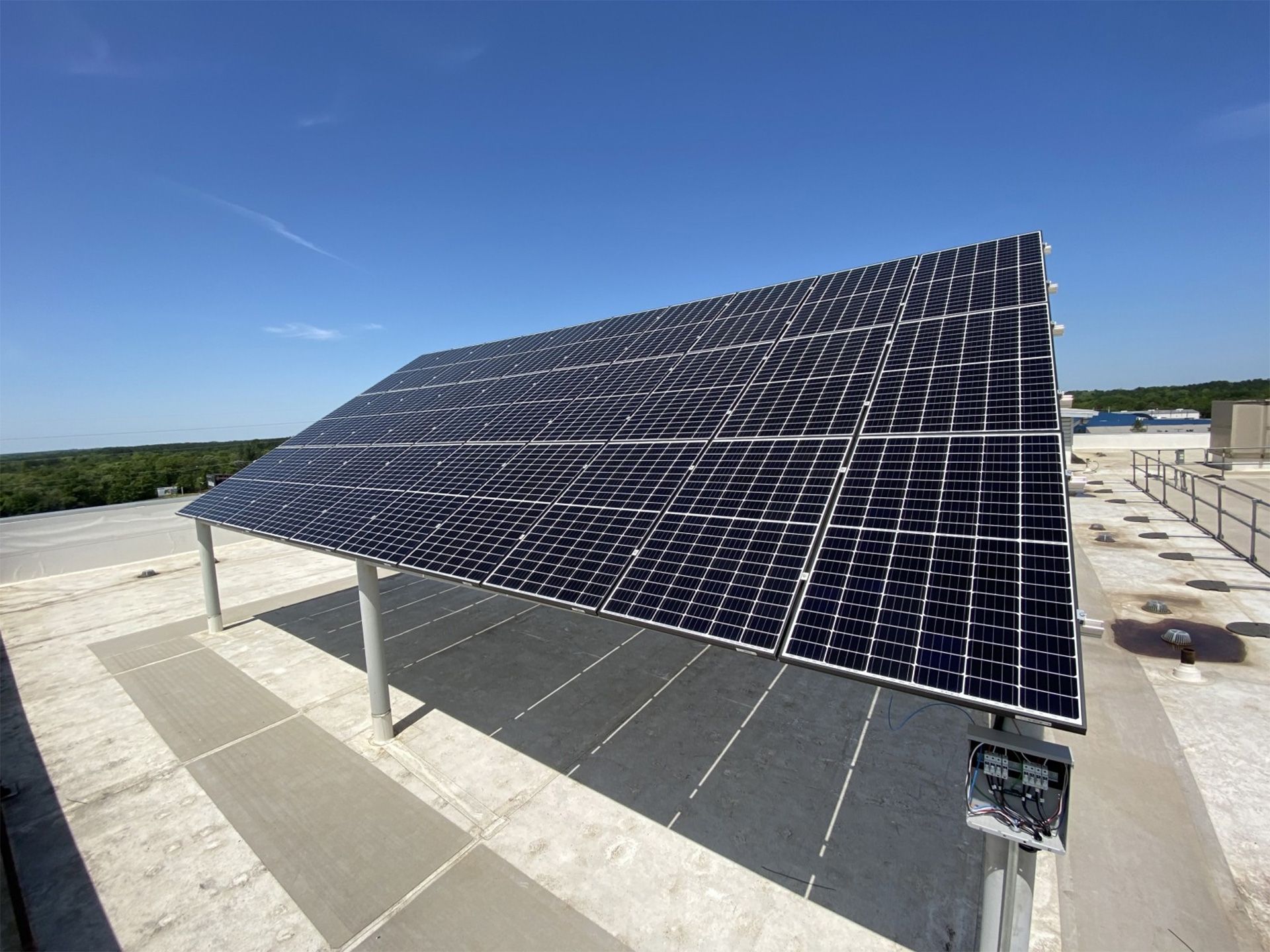A large, tilted solar panel array mounted on white pillars on a flat roof under a clear blue sky.