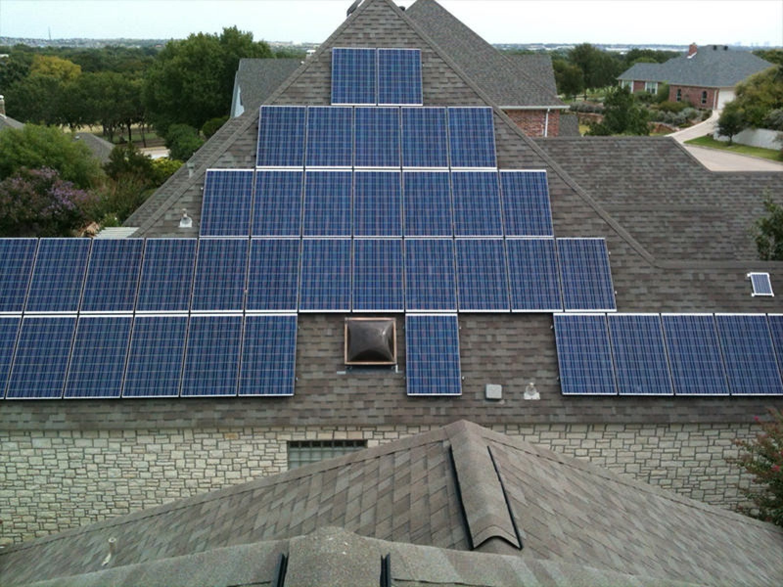 A large array of blue solar panels covering most of a dark gray shingled roof on a residential home.