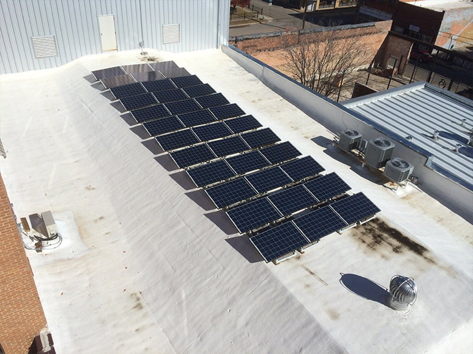 An aerial view of a rooftop featuring a rectangular array of black solar panels installed on a white flat roof.