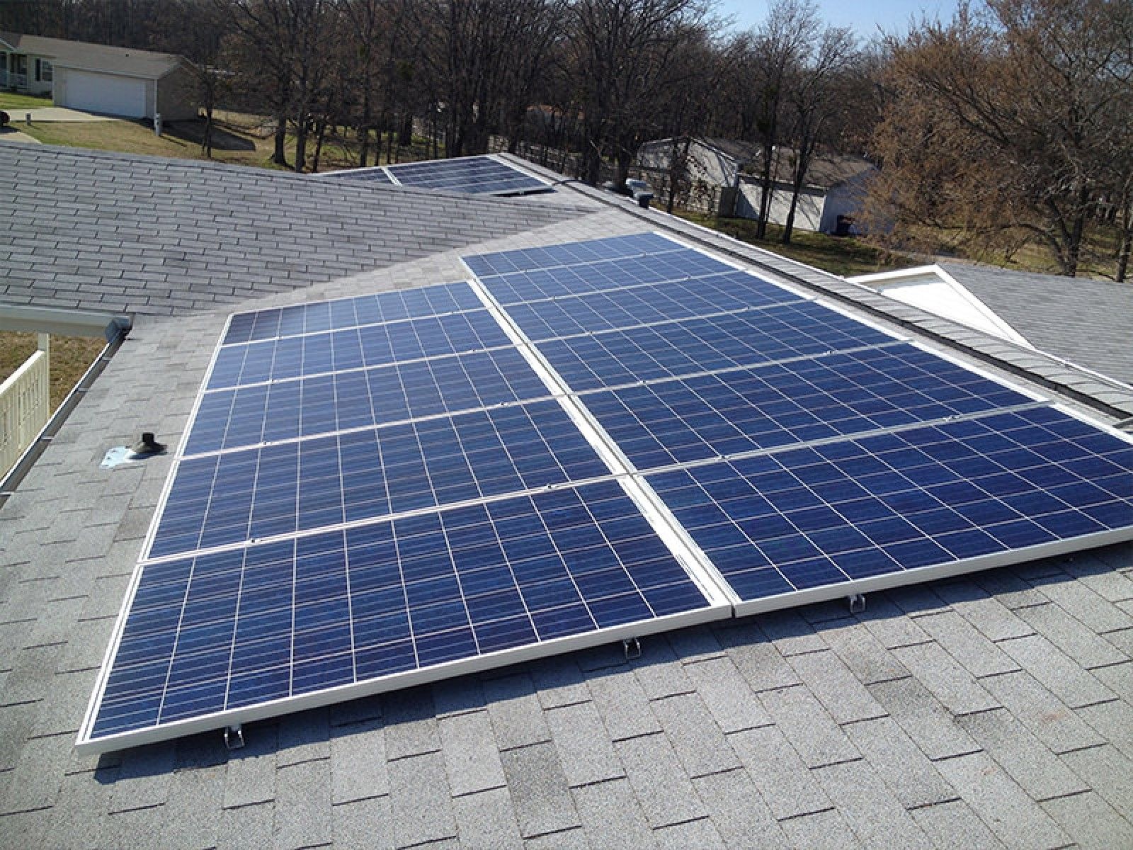 A rooftop installation of two rectangular arrays of blue solar panels on a gray shingled roof under a clear blue sky.