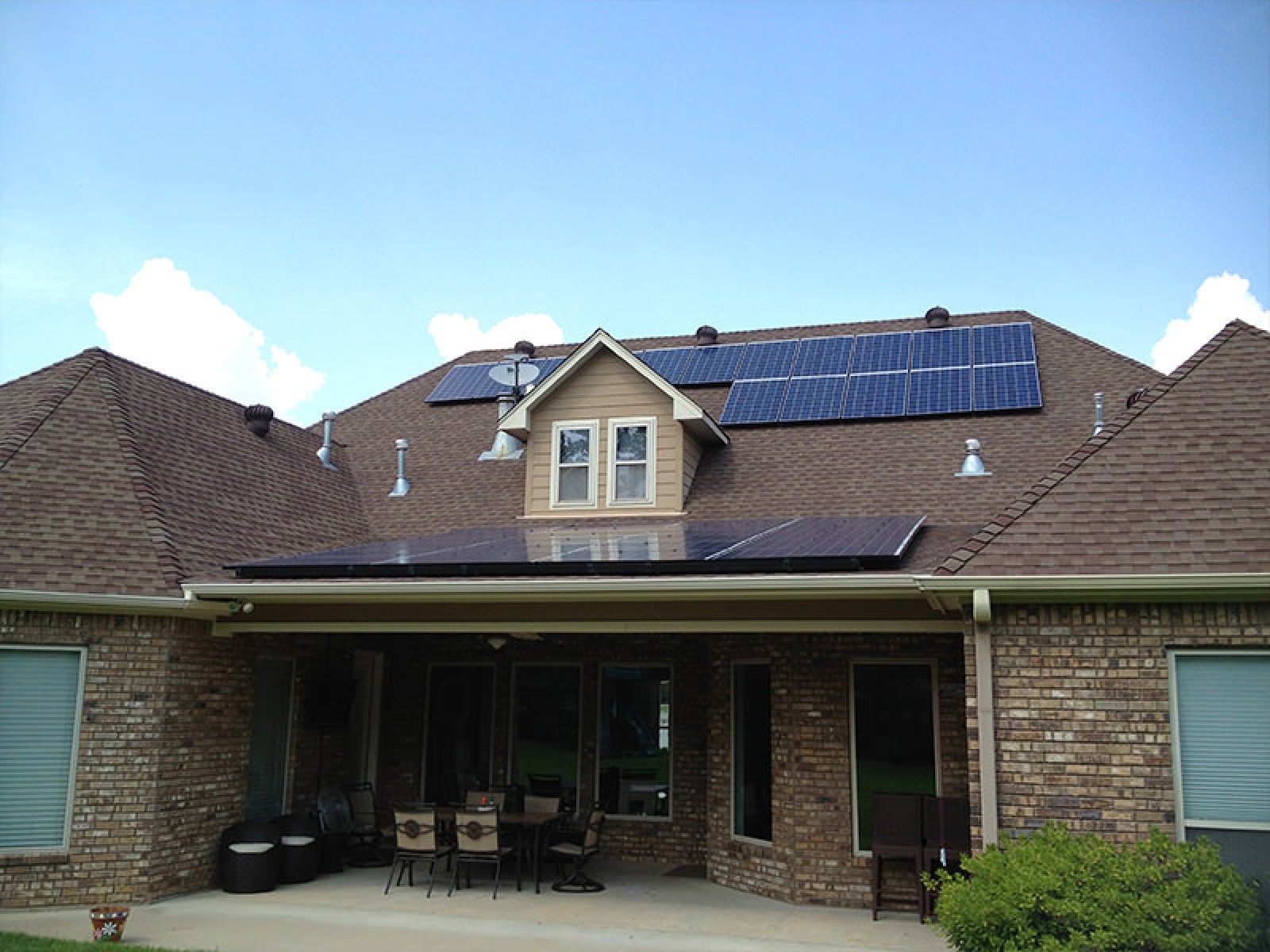 Back view of a brick house with solar panels installed on the roof and a patio area below.