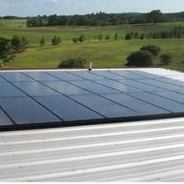 Solar panels installed on a metal roof overlooking a rural landscape with fields and trees.