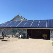 Solar panels installed on the roof of a house with a stone facade and an open garage door under a clear blue sky.