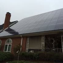 A brick house with a large solar panel array covering the entire roof, next to a tall brick chimney.