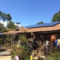 A rustic, wood-covered porch features decorative wall art, a metal gate, and a roof with solar panels under a blue sky.