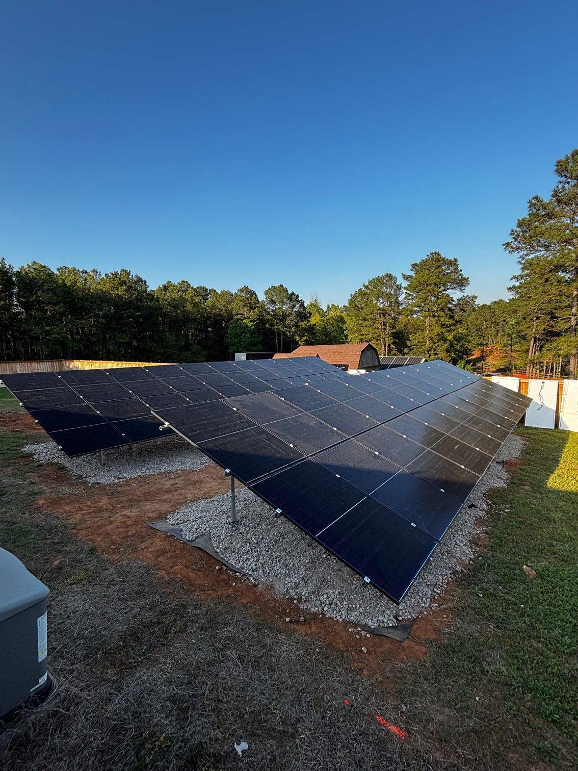 Ground-mounted solar panel array installed over a gravel bed in a sunny backyard with trees in the background.