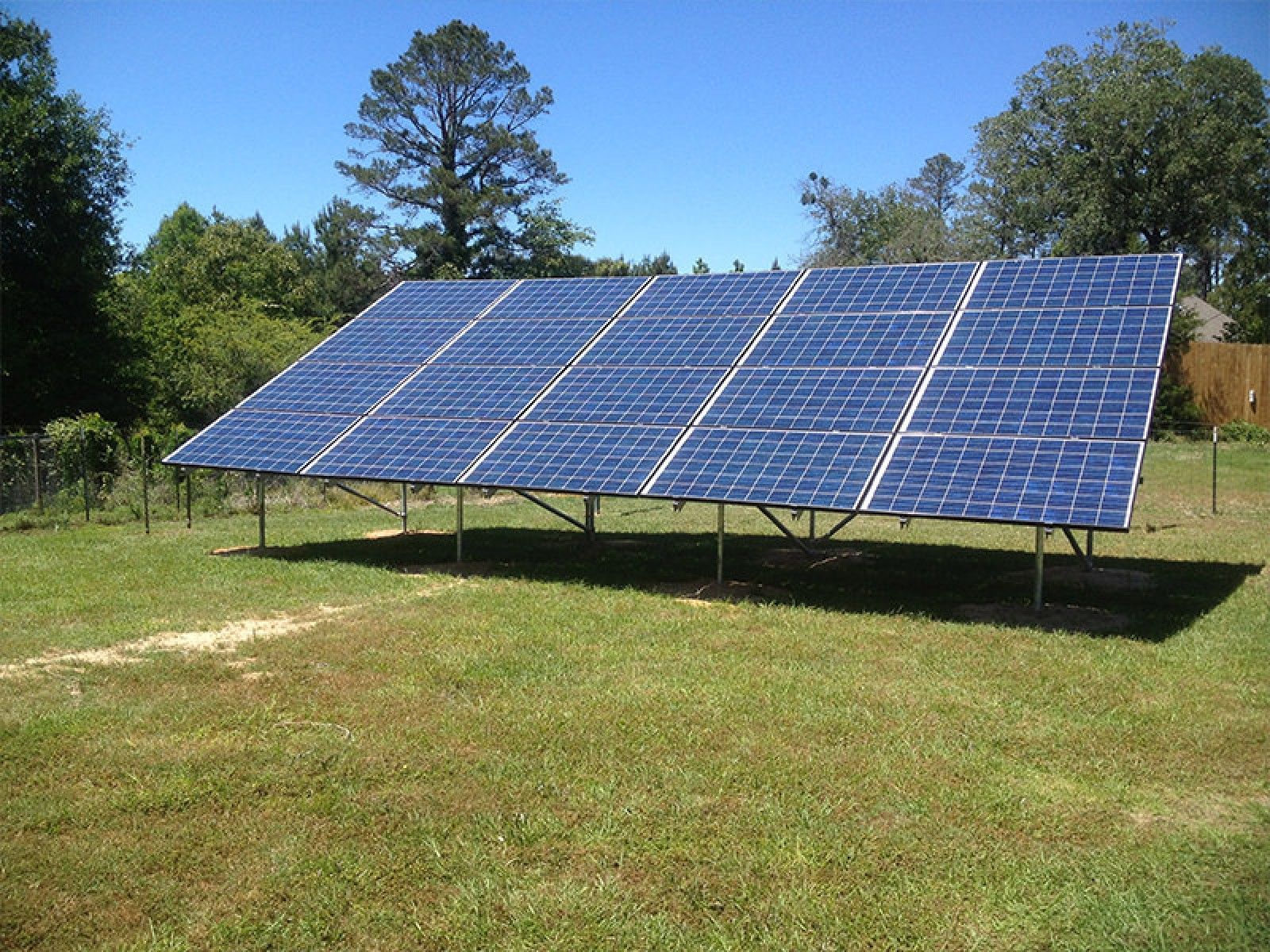 A ground-mounted solar panel array installed in a grassy field under a clear blue sky.