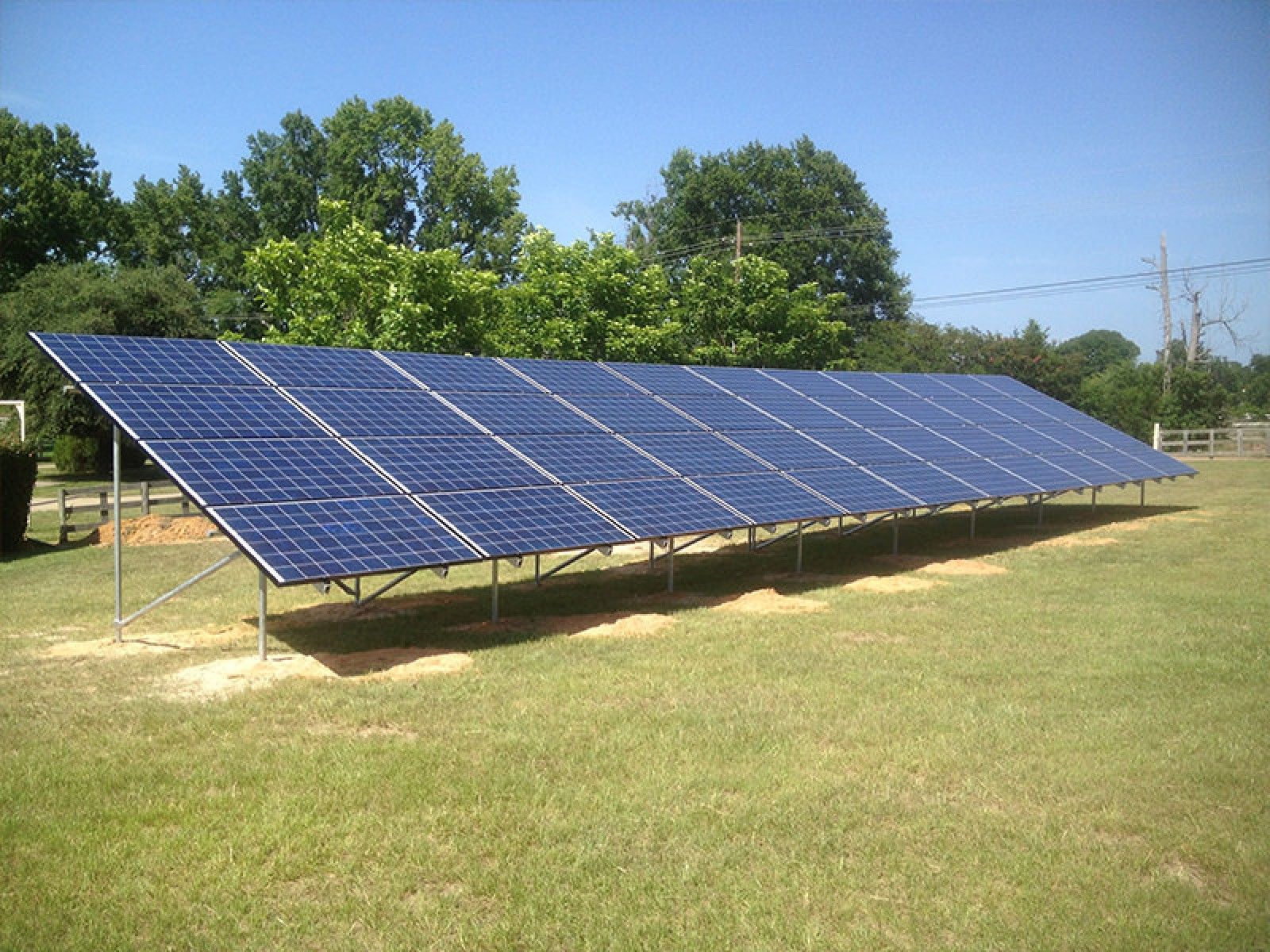 A ground-mounted solar panel array sits in a grassy field under a clear blue sky.