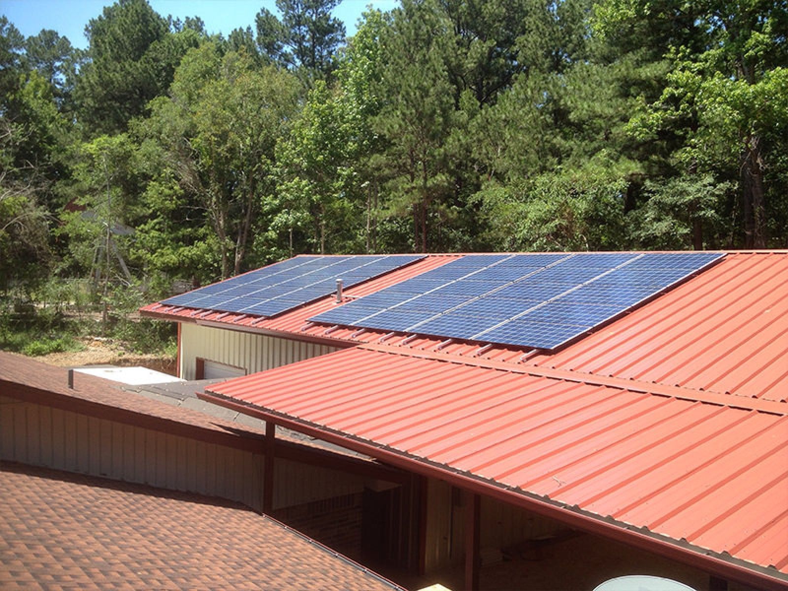 Solar panels installed on a red metal roof surrounded by green trees.