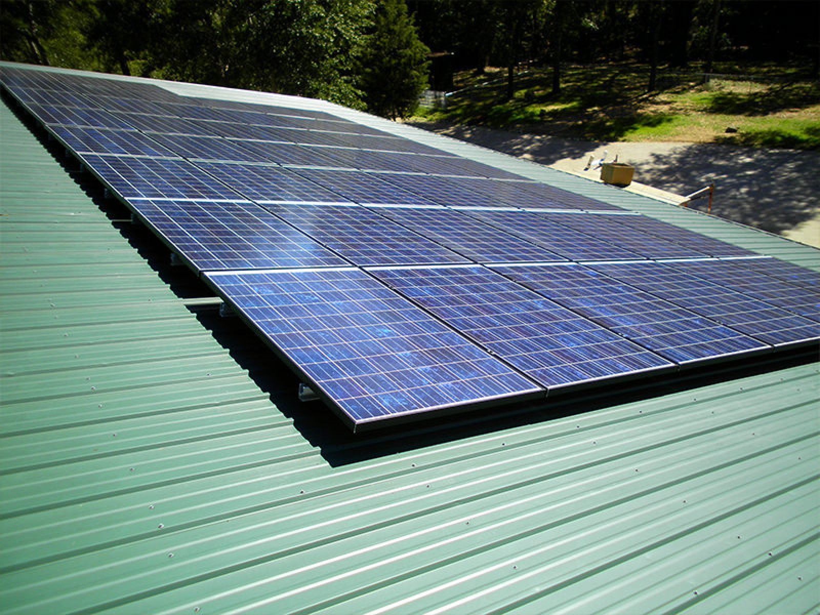A grid of solar panels mounted on a slanted, green corrugated metal roof outdoors.