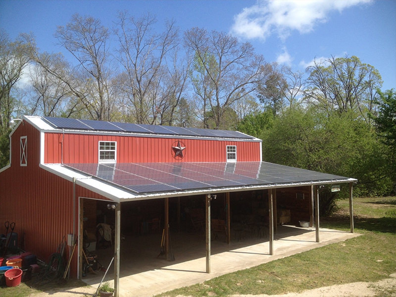 A red barn with a solar panel array mounted on its slanted roof, situated in a grassy area with trees in the background.