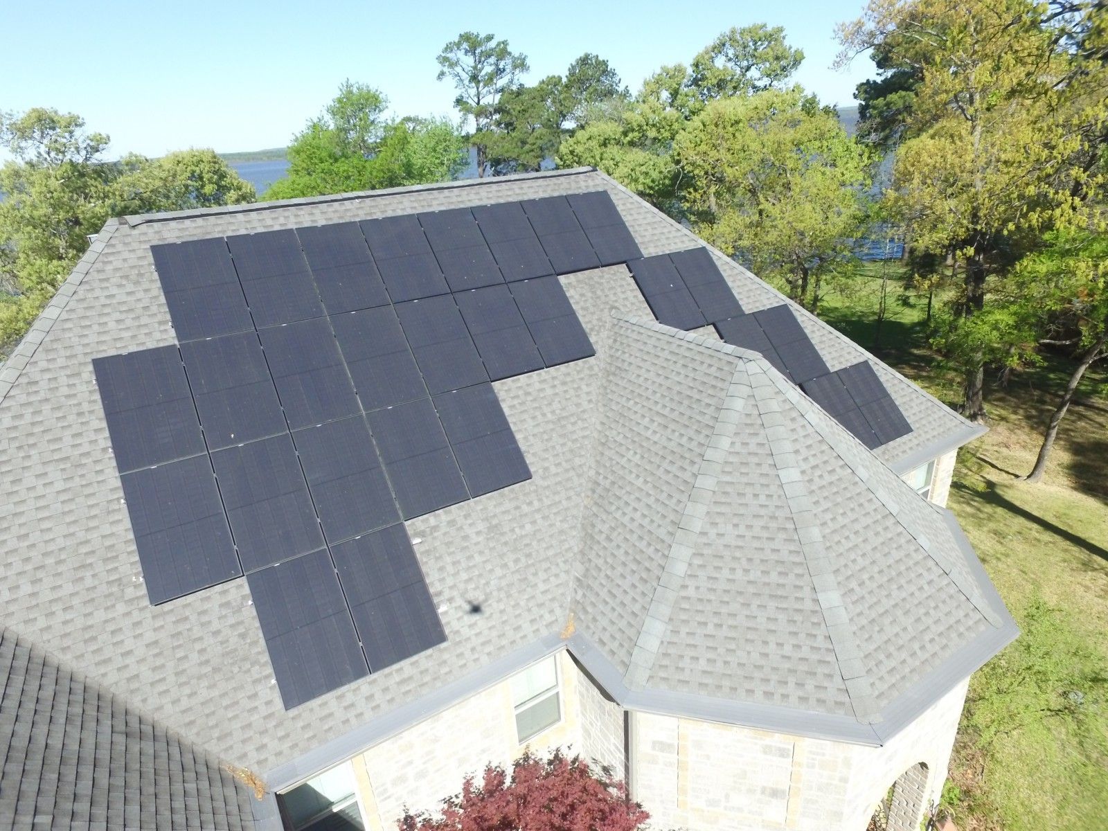 An aerial view of a residential roof featuring a large, multi-section array of black solar panels.